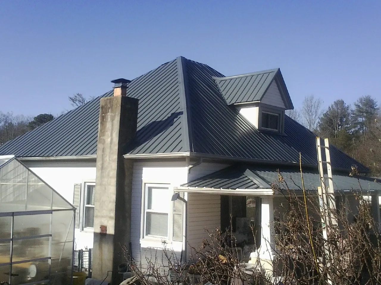 Dark blue standing seam metal roof on a white farmhouse with dormer — Slate & Tile Roof Repair by Roofing Brothers in Shepherdstown