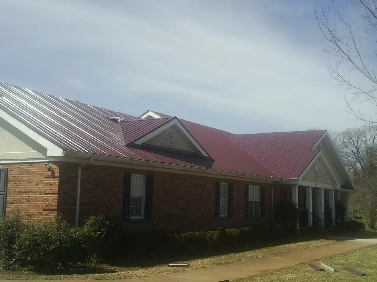 Red metal roof with gabled entries on a long brick building, from a Hail Damage Roof Repair job in Shepherdstown