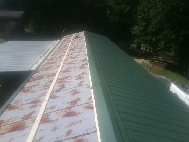 Old rusted panels beside newly installed green metal roofing — Wind Damage Roof Repair by Roofing Brothers in Shepherdstown