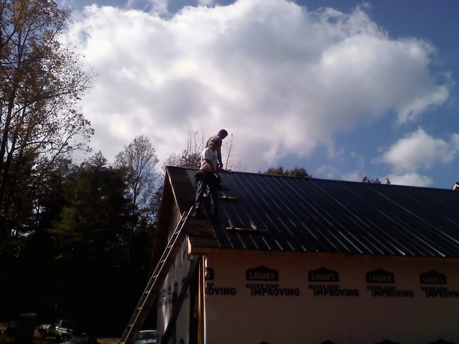 Roofer fastening dark metal panels high against a cloudy sky, from a Roof Inspection job in Shepherdstown