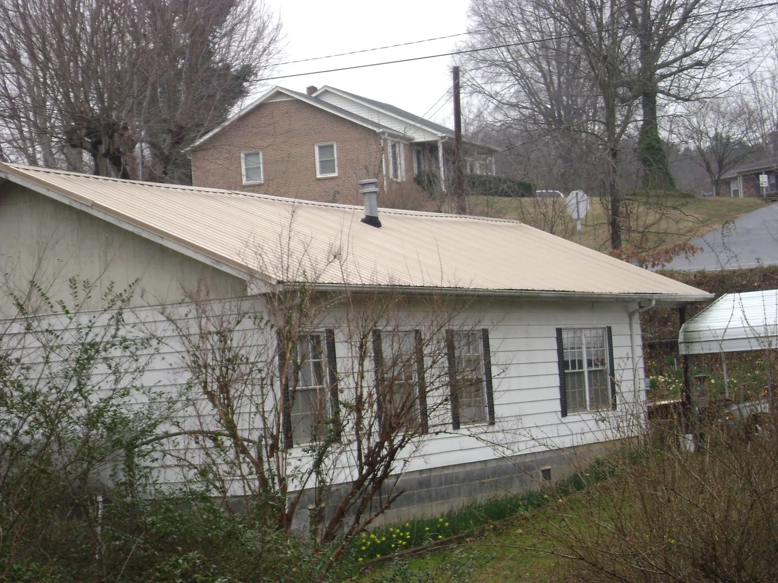 Tan metal roof on a white sided house set into a hillside — Commercial Roofing by Roofing Brothers in Shepherdstown